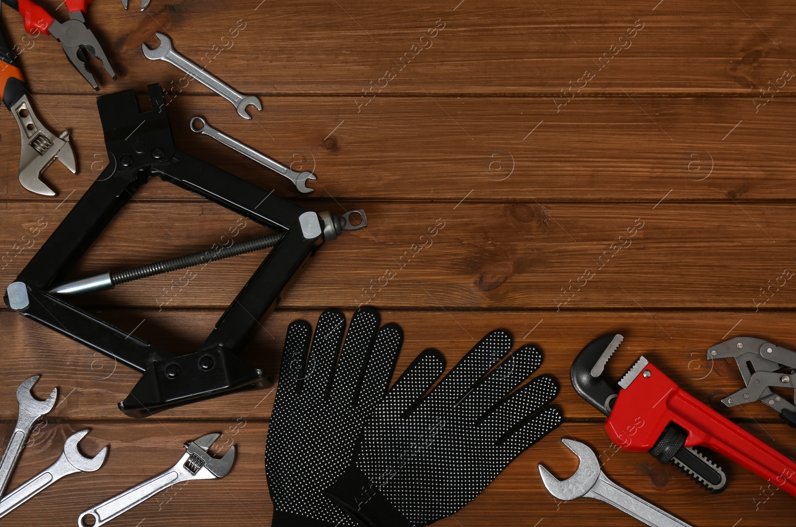 Photo of Car scissor jack, gloves and different tools on wooden surface, flat lay. Space for text