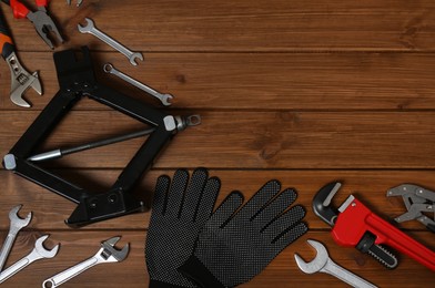 Photo of Car scissor jack, gloves and different tools on wooden surface, flat lay. Space for text