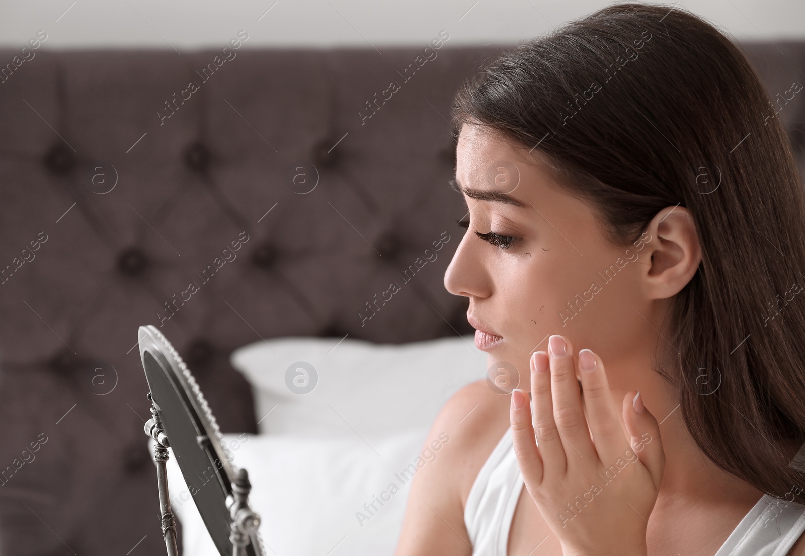 Photo of Young woman with eyelash loss problem looking in mirror indoors