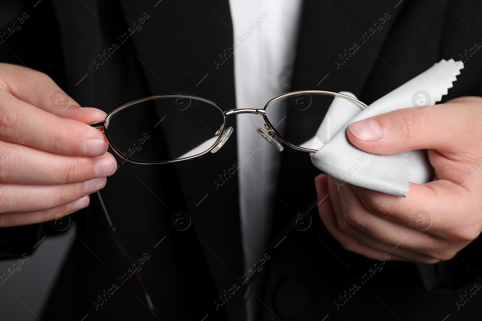 Photo of Woman wiping glasses with microfiber cloth on grey background, closeup