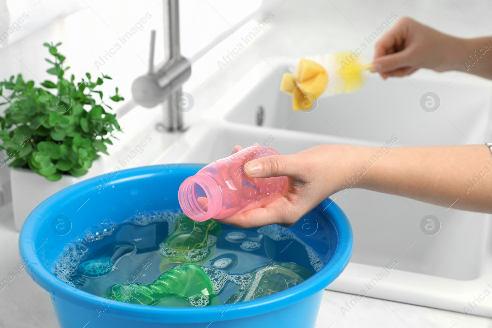 Photo of Woman washing baby bottle in kitchen, closeup