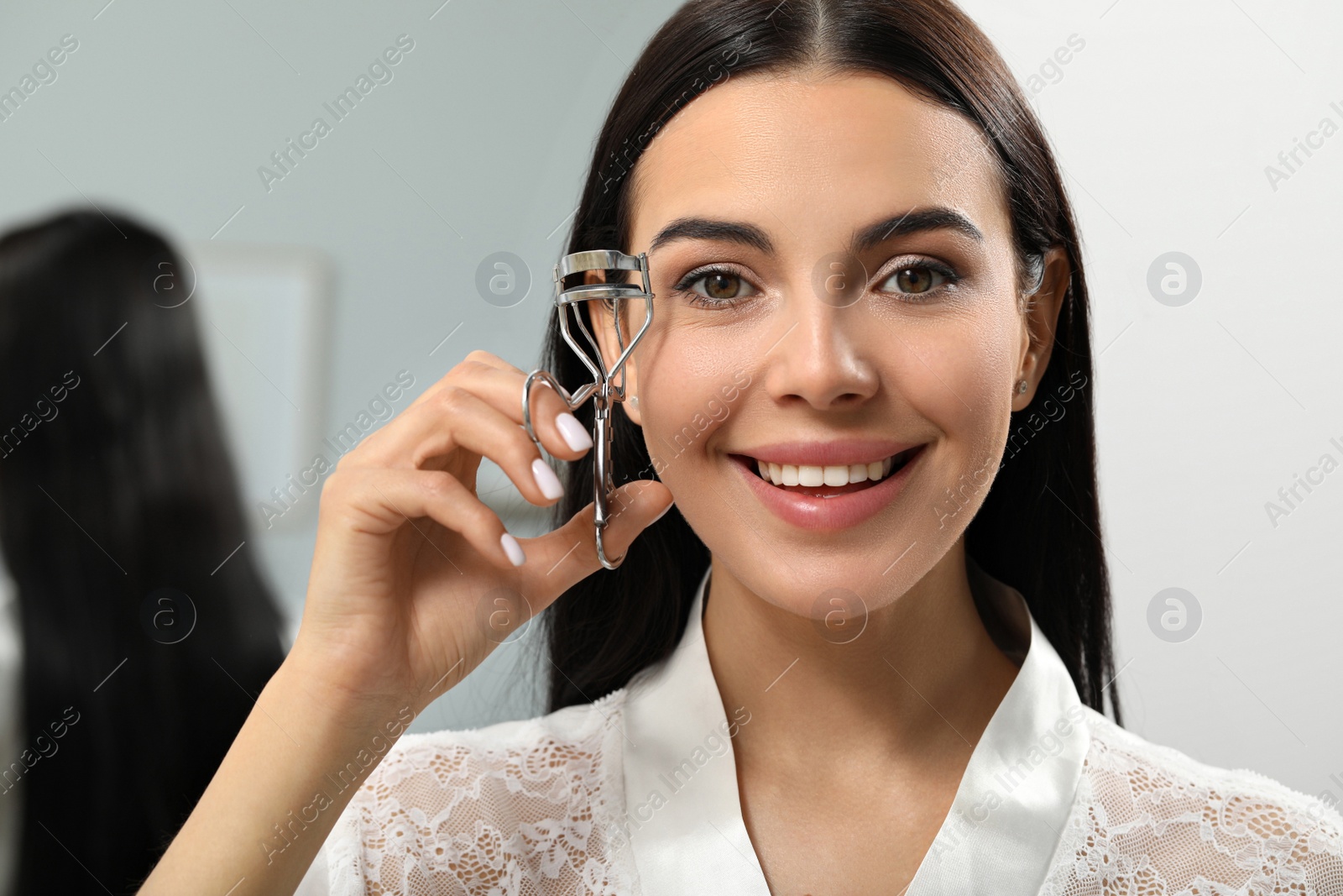 Photo of Beautiful young woman using eyelash curler indoors