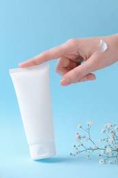 Woman with tube of cream and flowers on light blue background, closeup