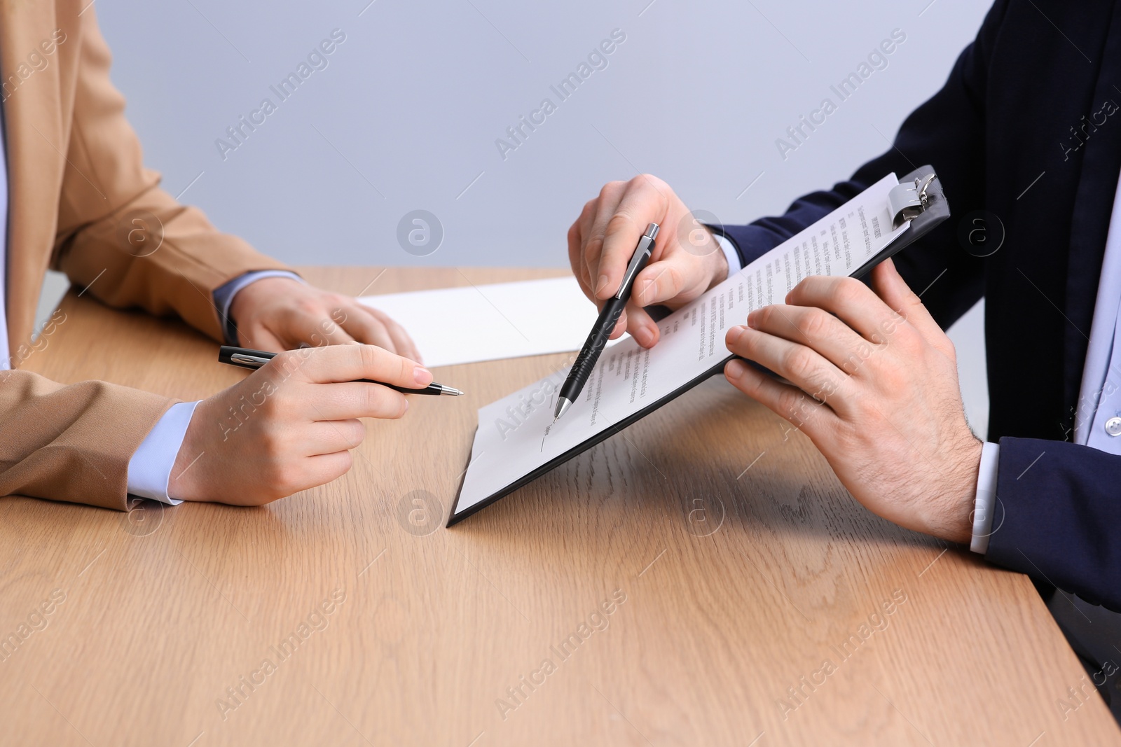 Photo of Businesspeople signing contract at wooden table, closeup of hands