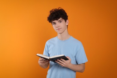 Photo of Portrait of teenage boy with book on orange background