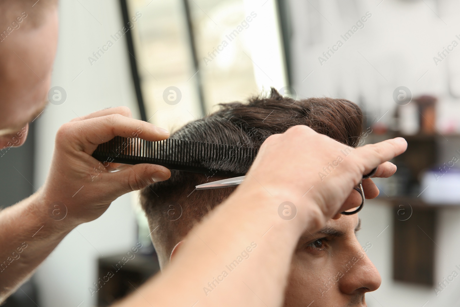 Photo of Professional barber making stylish haircut in salon, closeup