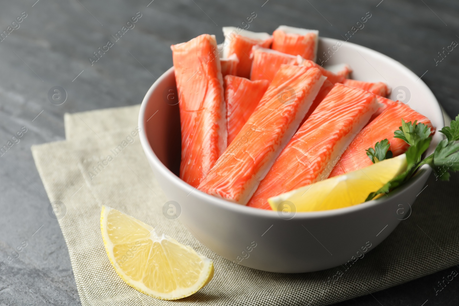 Photo of Crab sticks with lemon in bowl on grey table, closeup