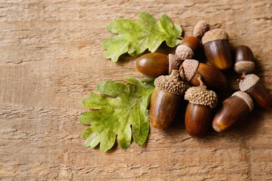 Pile of acorns and green oak leaves on wooden table. Space for text