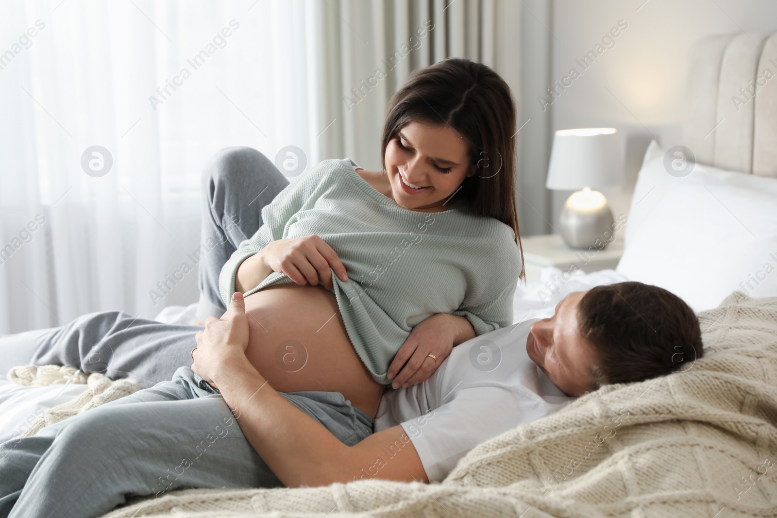 Photo of Young pregnant woman with her husband in bedroom