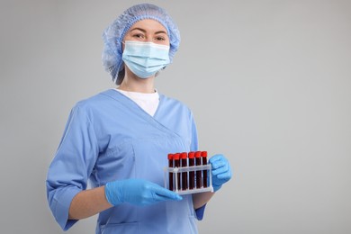Photo of Laboratory testing. Doctor with blood samples in tubes on light grey background, space for text