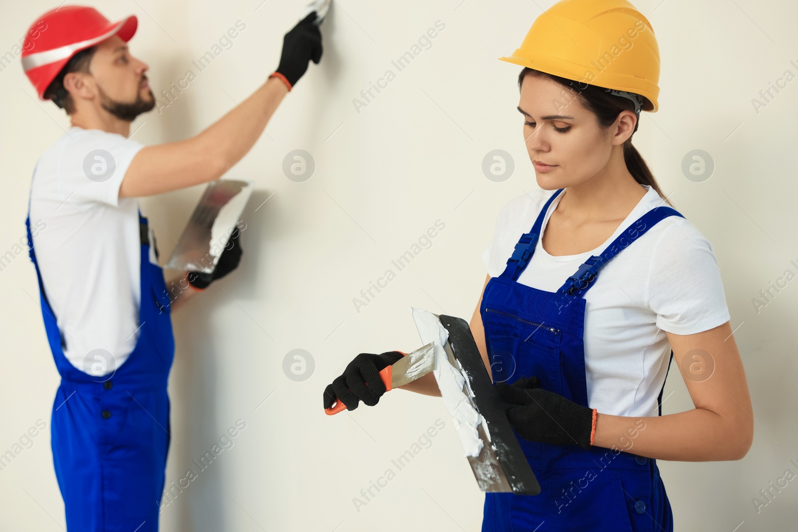 Photo of Professional workers with putty knives in hard hats near wall
