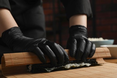 Photo of Chef in gloves making sushi roll at wooden table, closeup