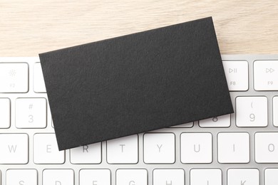 Photo of Blank black business card and computer keyboard on wooden table, top view. Mockup for design