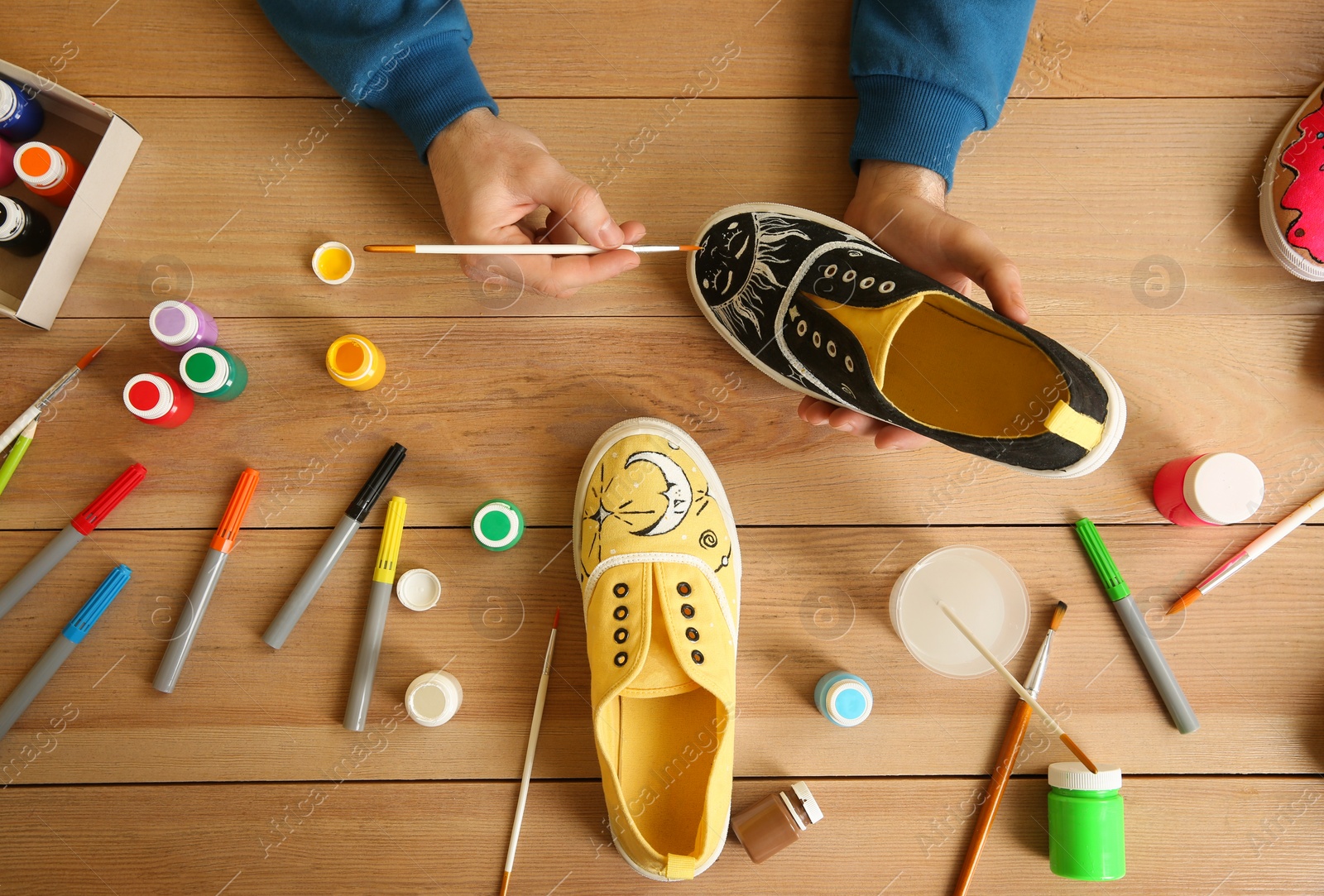 Photo of Man painting on sneaker at wooden table, top view. Customized shoes