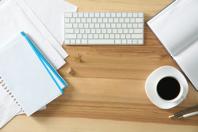 Modern computer keyboard, cup of coffee and office supplies on wooden table, flat lay. Space for text