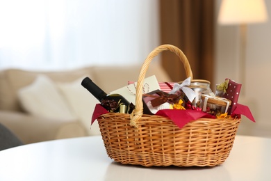 Photo of Wicker basket full of gifts on white table in living room