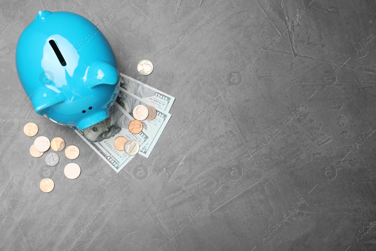 Photo of Top view of piggy bank and cash on grey stone table, space for text. Money savings