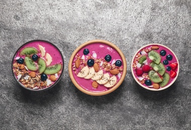 Photo of Acai smoothie bowls with granola and fruits on grey table, flat lay