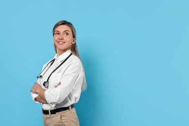 Portrait of happy doctor with stethoscope on light blue background, space for text