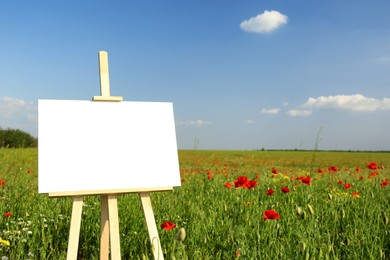 Photo of Wooden easel with blank canvas in poppy field on sunny day