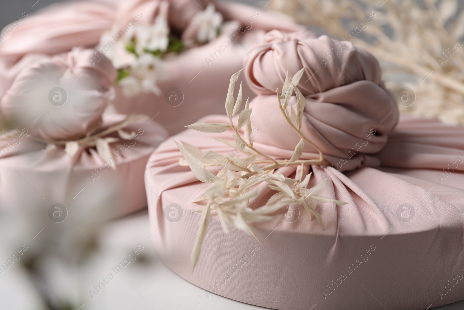 Photo of Furoshiki technique. Gifts packed in pink fabric and dried branches on white table, closeup