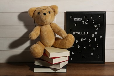 Black letter board with word Dyslexia, books and teddy bear on wooden table near white wall