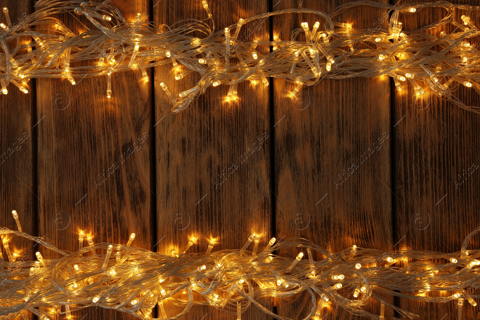 Photo of Glowing Christmas lights on wooden background, top view. Space for text