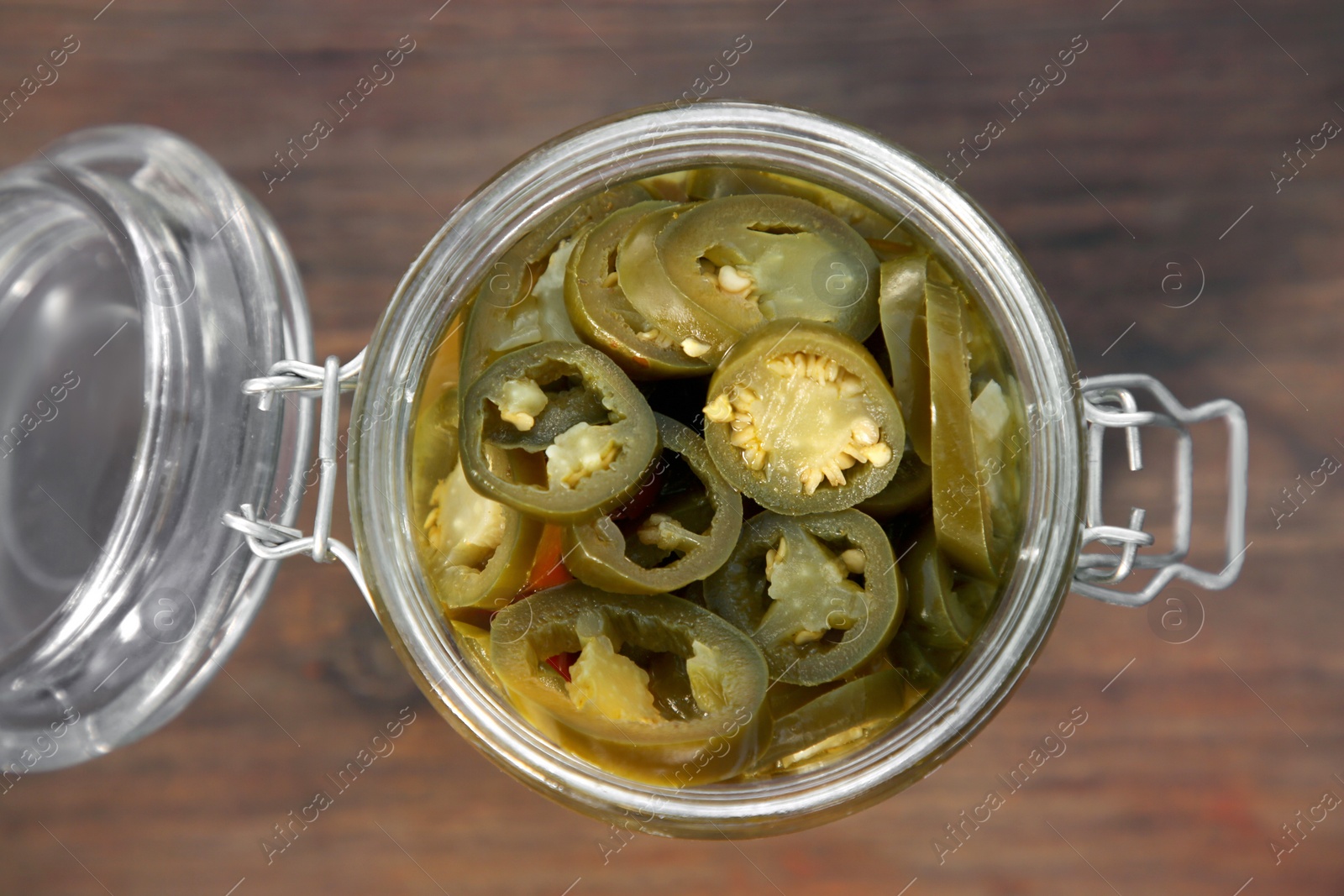 Photo of Glass jar of pickled green jalapeno peppers on wooden table, top view