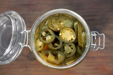 Photo of Glass jar of pickled green jalapeno peppers on wooden table, top view