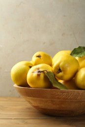 Tasty ripe quince fruits in bowl on wooden table, closeup