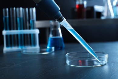 Photo of Laboratory analysis. Micropipette with liquid and petri dish on black table