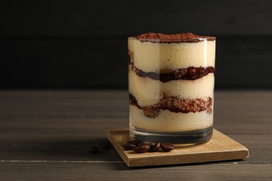 Delicious tiramisu in glass and coffee beans on wooden table, closeup. Space for text