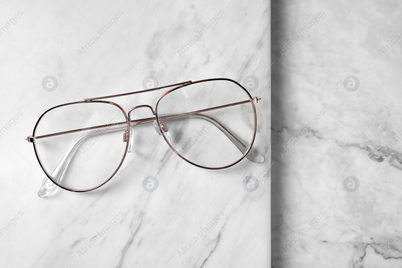 Photo of Glasses in stylish frame on white marble background, top view. Space for text