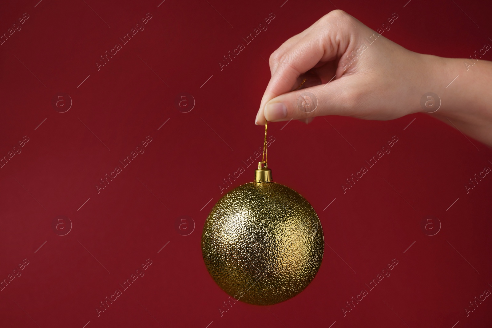 Photo of Woman holding golden Christmas ball on red background, closeup. Space for text