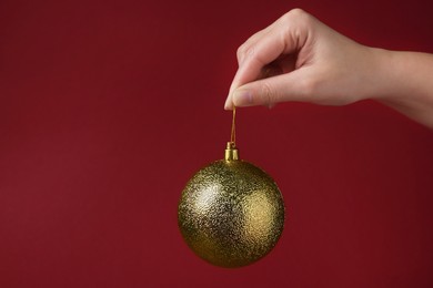 Woman holding golden Christmas ball on red background, closeup. Space for text