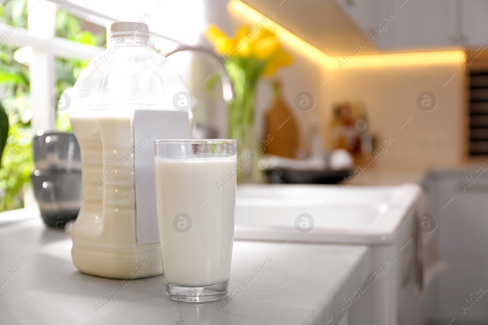 Photo of Gallon bottle of milk and glass on white countertop in kitchen. Space for text