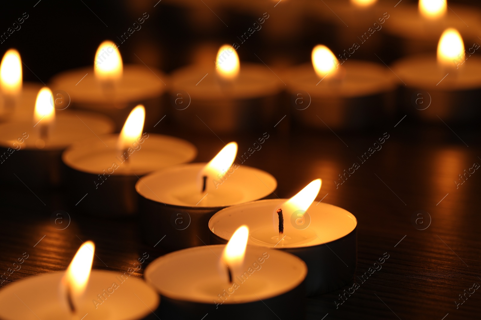 Photo of Burning tealight candles on dark surface, closeup