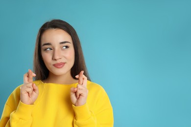 Woman with crossed fingers on light blue background, space for text. Superstition concept