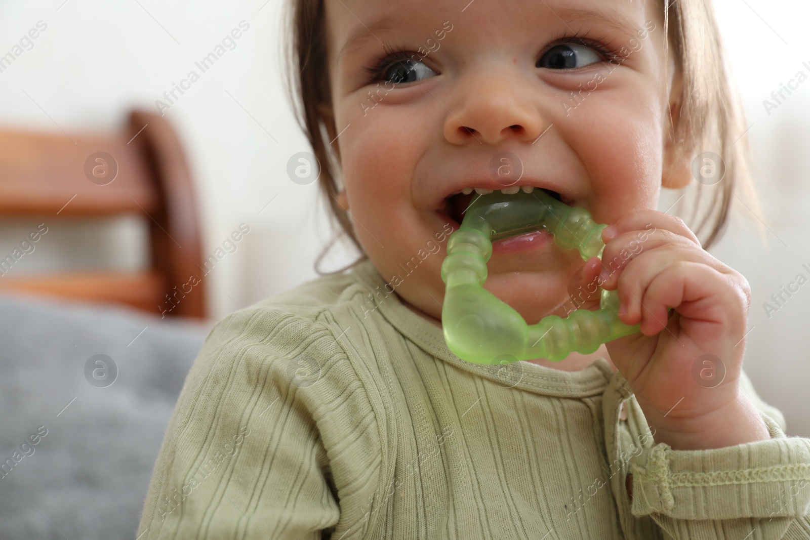 Photo of Cute baby girl with teething toy at home, closeup