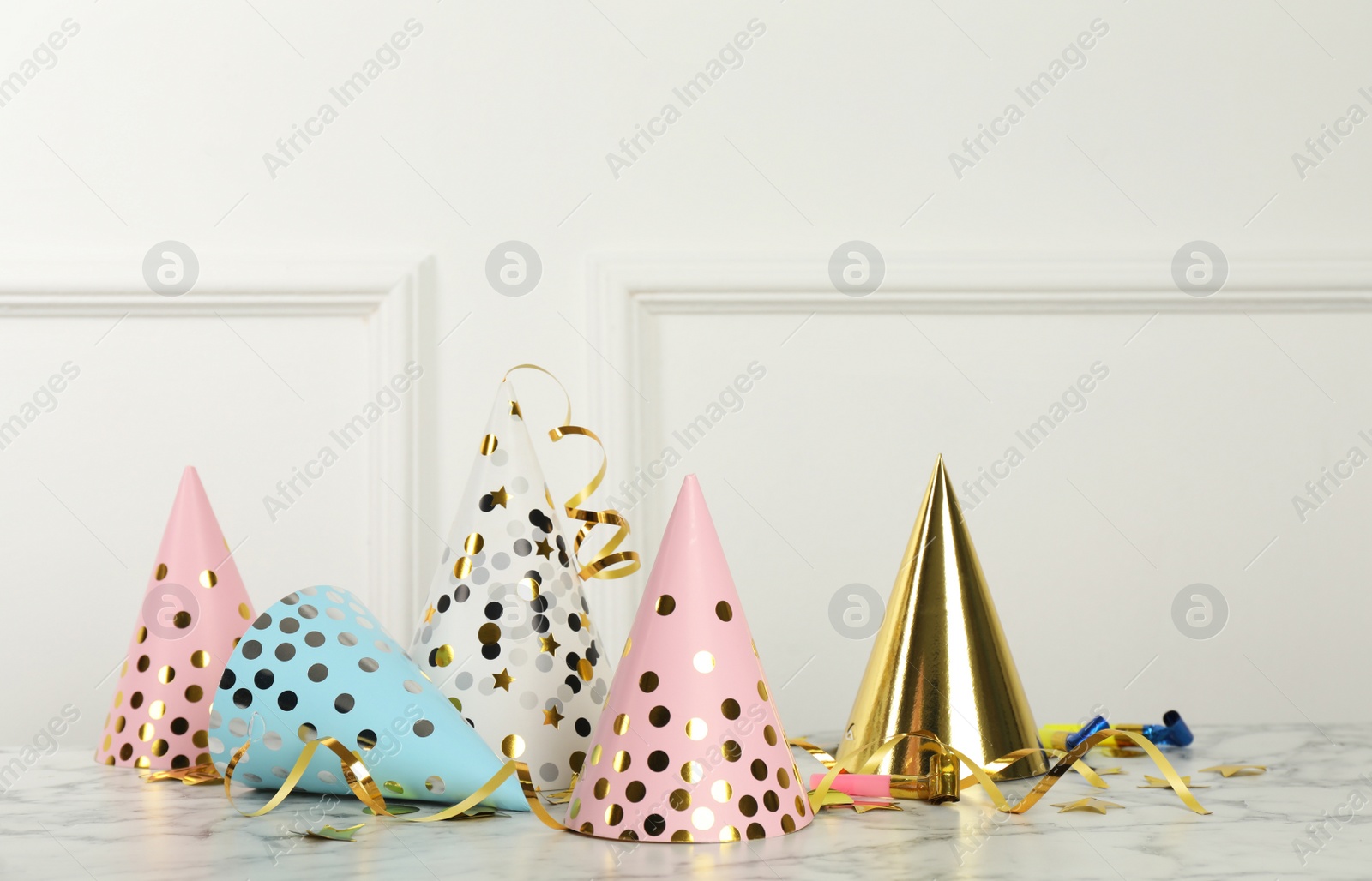 Photo of Party hats and festive items on marble table near white wall indoors. Space for text