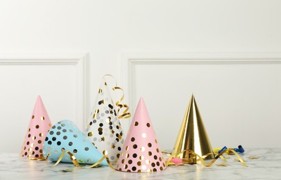 Party hats and festive items on marble table near white wall indoors. Space for text