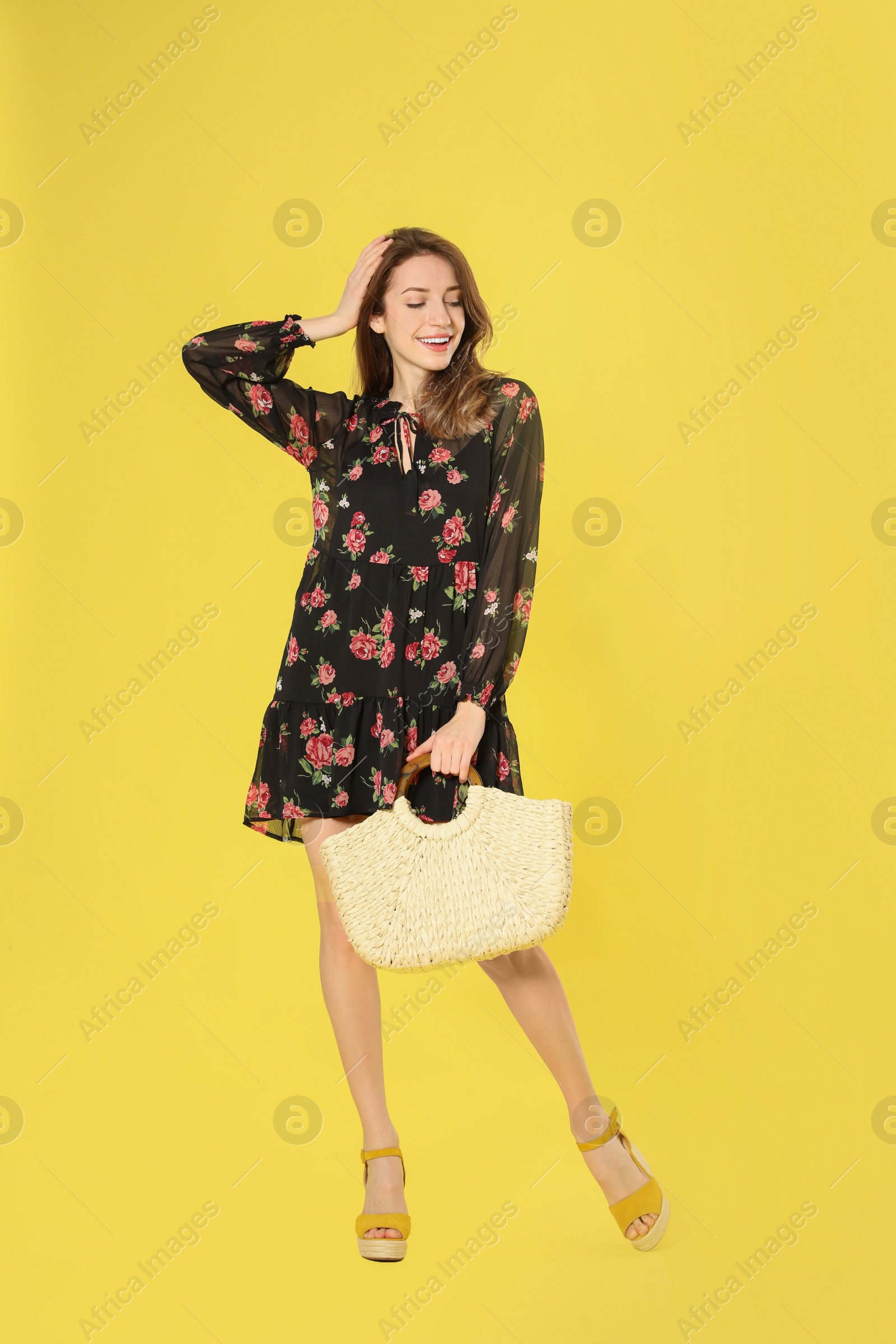 Photo of Young woman wearing floral print dress with straw bag on yellow background