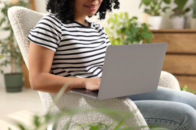 Photo of Relaxing atmosphere. Happy woman with laptop sitting in armchair near houseplants at home, closeup
