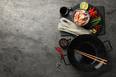 Flat lay composition with black wok, spices and products on dark textured table. Space for text