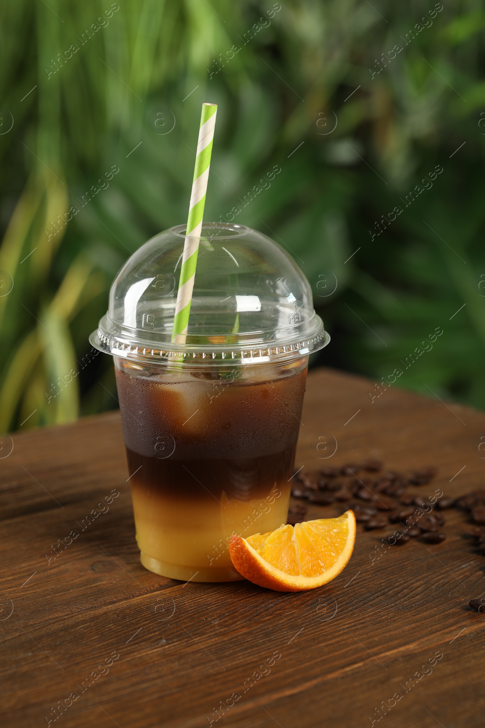 Photo of Tasty refreshing drink with coffee and orange juice in plastic cup on wooden table against blurred background