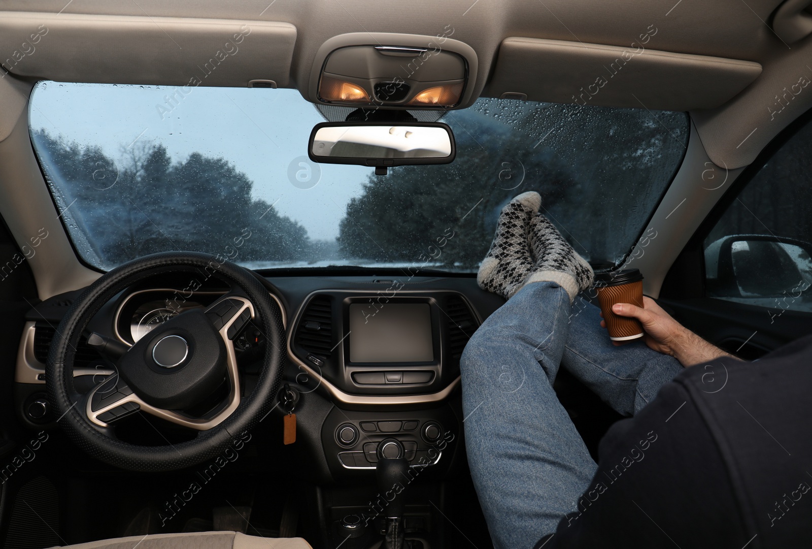 Photo of Young man in warm socks with coffee resting inside car, closeup