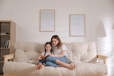 Photo of Mother and daughter reading book on sofa at home