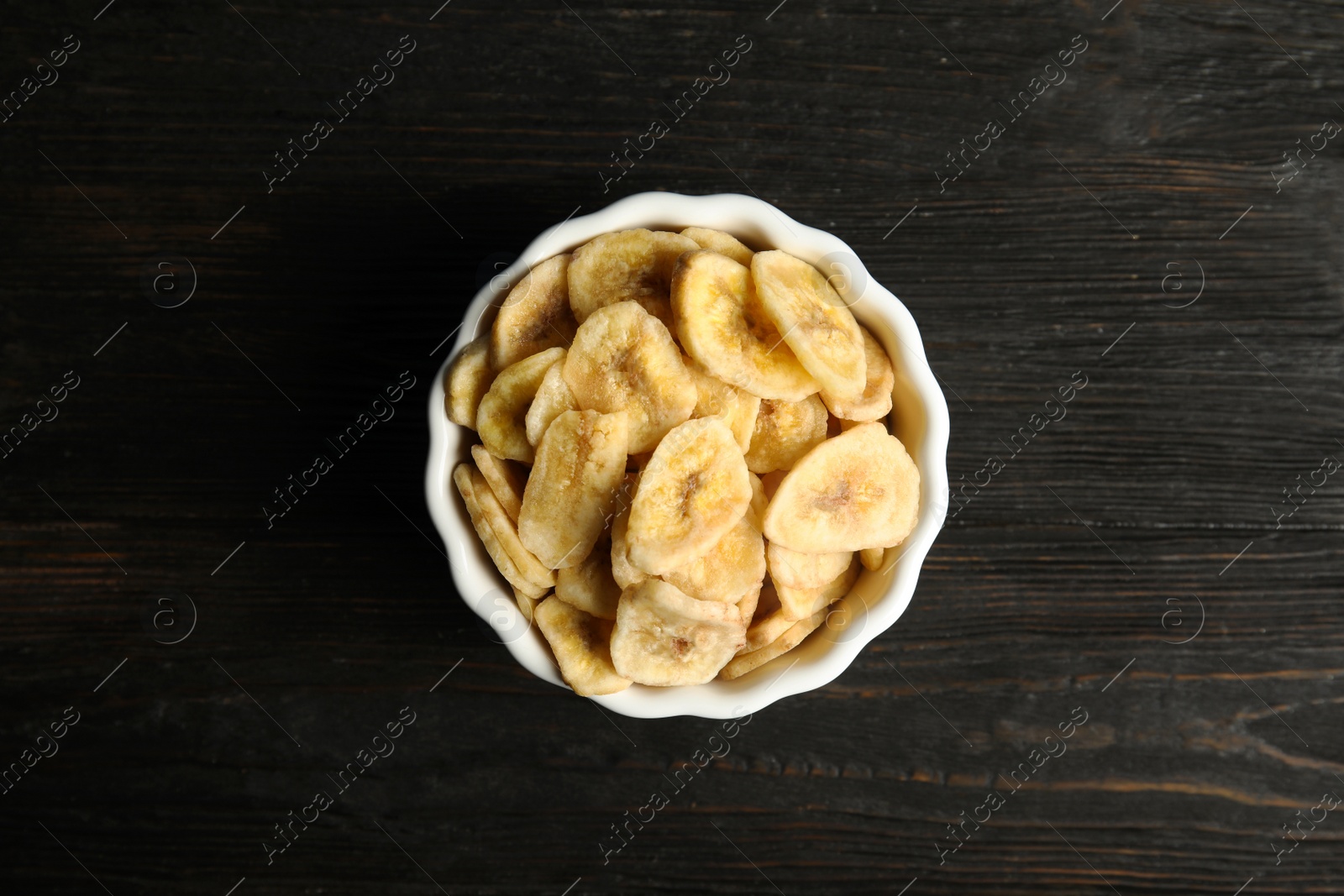 Photo of Bowl with sweet banana slices on wooden  table, top view. Dried fruit as healthy snack