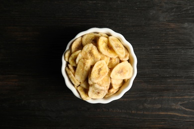 Photo of Bowl with sweet banana slices on wooden  table, top view. Dried fruit as healthy snack