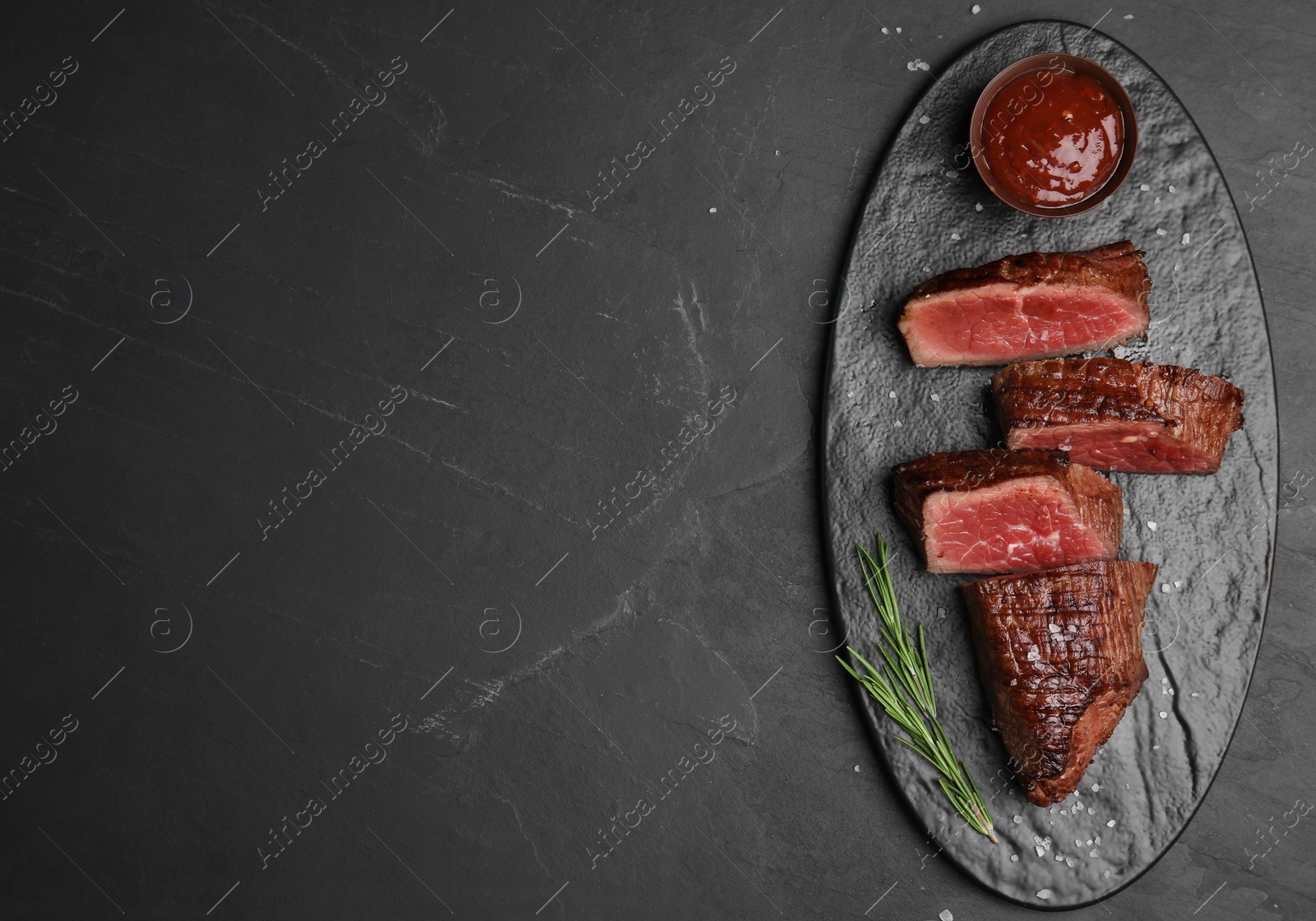 Photo of Delicious sliced beef tenderloin on black table, top view. Space for text